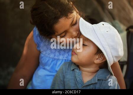 Die große Schwester tröstet ihren kleinen Bruder, nachdem er im Freien verletzt wurde, indem sie ihm einen Kuss auf die Stirn gibt. Stockfoto