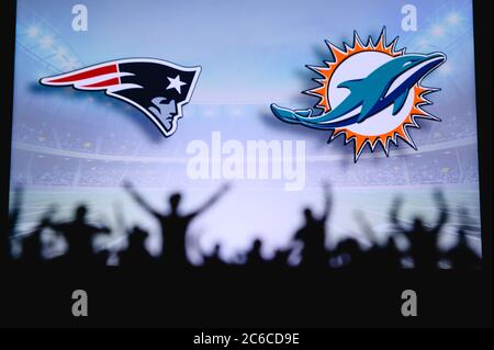 New England Patriots gegen Miami Dolphins. Fans unterstützen NFL Game. Silhouette der Unterstützer, große Leinwand mit zwei Rivalen im Hintergrund. Stockfoto