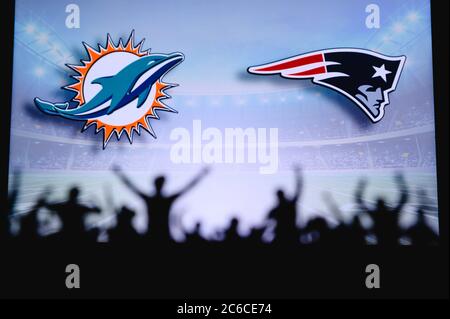 Miami Dolphins gegen New England Patriots. Fans unterstützen NFL Game. Silhouette der Unterstützer, große Leinwand mit zwei Rivalen im Hintergrund. Stockfoto