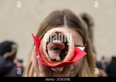 Die junge Frau guckelt durch einen traditionellen Trdelnik, ein tschechisches süßes Gebäck, das auf den Weihnachtsmärkten sehr beliebt ist Stockfoto