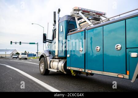 Leistungsstarke schwere Big-Rig mobile Abschleppwagen mit Notbeleuchtung und Abschleppausrüstung läuft auf der Stadtstraße mit Ampel geht zu ihm Stockfoto