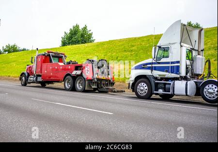 Leistungsstarke schwere Big-Rig mobile Abschleppwagen mit Notlicht und Abschleppausrüstung Vorbereitung zum Abschleppen gebrochenen weißen Big-Rig-Semi-Traktor stehend Stockfoto