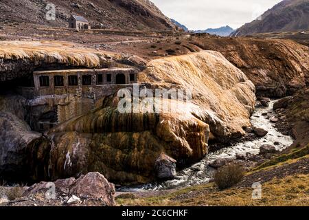 Panoramablick auf den Bach, der unter den Thermalbädern auf der Inka-Brücke mit einer Kapelle und die braunen Berge im Hintergrund auf einer Wolke passiert Stockfoto