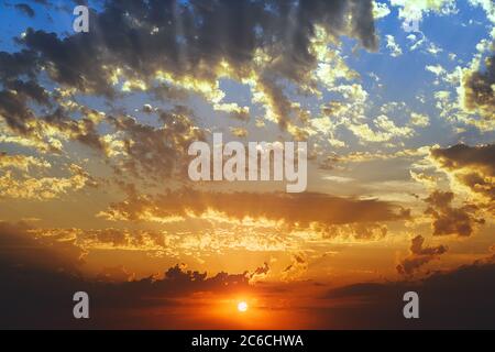 Sonnenstrahl beleuchtet die Wolken während des Sonnenuntergangs mit dem blauen Himmel hinter Stockfoto