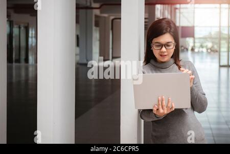 Frau im Büro hat Videogespräch. Junge positive Frau in Brille vor dem Laptop stehen und mit jemandem online sprechen. Stockfoto