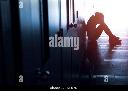 Silhouette eines deprimierten Mannes, der auf dem Gang des Gebäudes sitzt. Trauriger Mann, Schrei, Drama, einsam und unglücklich Konzept. Stockfoto