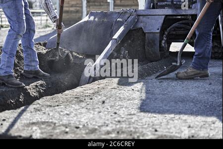 Nahaufnahme einer Grabenschaufelkette in Bewegung Graben einen Graben in Schmutz mit Arbeitern schaufeln zur Seite Stockfoto