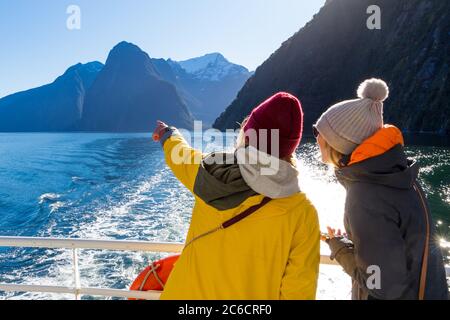 Weibliche Touristen an Bord eines Kreuzfahrtschiffes im Milford Sound zeigen in Richtung Mitre Peak, Fiordland National Park, Neuseeland Stockfoto