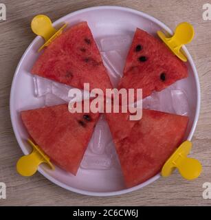 Wassermelonenscheiben in einer Schüssel mit Eis auf einem Eisstock auf einem Holzhintergrund. Kreative Idee Stockfoto