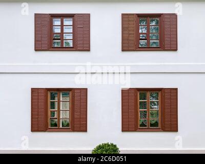 Weiße Außenwand aus Gipsholz mit braunen Fenstern und hölzernen Fensterläden Stockfoto