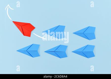 Rotes Papierflugzeug, das aus der Reihe heraus fliegt, führt blaue Flugzeuge. Konzept für neue Geschäftsstrategien, Führung, Entdeckung und anderes Denken Stockfoto