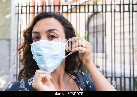 Junge Frau, die auf der Straße eine chirurgische Maske aufsetzt, um sich zu schützen und hygienische Sicherheitsmaßnahmen zu treffen. Konzept von Schutz und Sicherheit Stockfoto