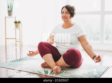 Erwachsene charmante Brünette Frau plus Größe Körper positive Praxis Yoga im hellen Studio Stockfoto