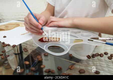 Kaffeezeichnungen. Mädchen zeichnet eine Kaffeetasse mit Kaffee statt Farben Stockfoto