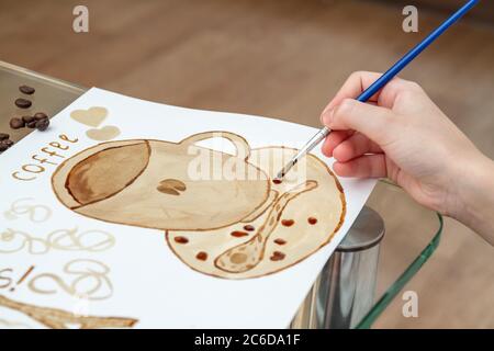Kaffeezeichnungen. Mädchen zeichnet eine Kaffeetasse mit Kaffee statt Farben Stockfoto