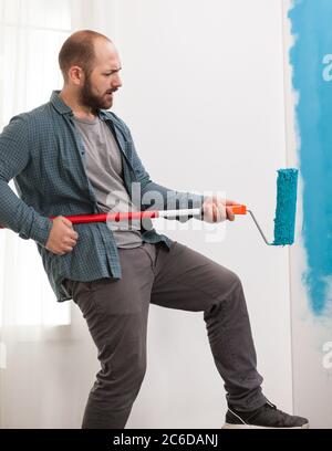 Reparaturman während des Hausbaus mit Roller Pinsel als Gitarre. Kerl singen während der Renovierung Haus. Wohnung Renovierung und Hausbau während der Renovierung und Verbesserung. Reparatur und Dekoration. Stockfoto