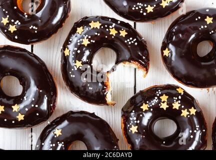 Donuts mit Schokoladenspiegel Vereisung und Streuseln auf weißem Holzhintergrund. Draufsicht. Stockfoto