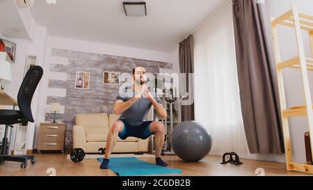 Athletischer Mann trainiert seine Beine dabei hocken Übung zu Hause. Stockfoto