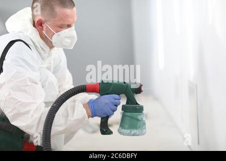 Mann in Maske hält Spritzpistole in den Händen und malt die Wand Stockfoto