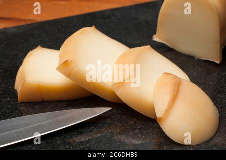 Scheiben geräucherter Scamorza, typisch italienischer Käse auf einem schwarzen Granitbrett, das auf einem Holztisch ruht Stockfoto