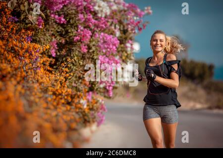 Sportliche Frau auf dem Workout unter schönen blühenden Blumen. Aktive Frauen laufen im Freien und Musik hören. Gewichtsverlust. Happy Healthy Life Stockfoto