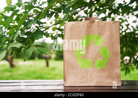 Leere Papiertüte steht auf einem Holztisch vor dem Hintergrund grüner Blätter. Einkaufskonzept. Speicherplatz kopieren. Stockfoto