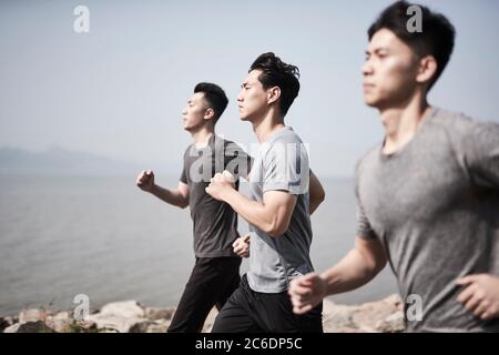 Drei junge asiatische Erwachsene Männer laufen Joggen im Freien am Meer Stockfoto