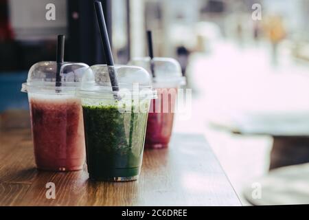 Süßer Smoothie in Plastikbechern auf Holztisch Stockfoto