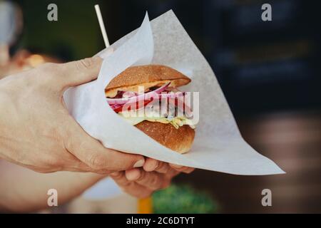 Junger Mann im weißen T-Shirt in den Händen halten Fast-Food-Burger, amerikanische Mahlzeit auf schwarzem Hintergrund. Stockfoto