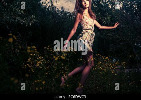 Fröhliches Mädchen. Ein junges Mädchen trägt ein leichtes Sommerkleid und tanzt in der Nacht im hohen Gras Stockfoto