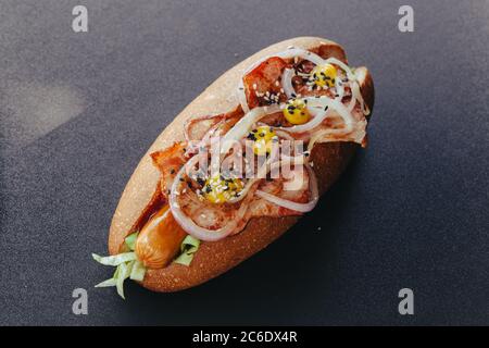 Großes Hotdog mit Wurst, Tomaten, Senf und Salat auf schwarzen Hintergrund isoliert. Ansicht von oben. Stockfoto