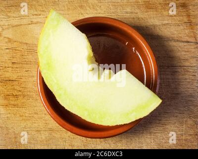 Eine Scheibe frische galia Melone in einer kleinen braunen Schale auf einem Holzschneidebrett Stockfoto