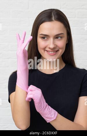 Junge Frau Kosmetologin und Brauen Spezialist setzt auf Schutzhandschuhe und eine Maske, um mit einem Kunden, Hygiene in einem Schönheitssalon zu arbeiten. Stockfoto