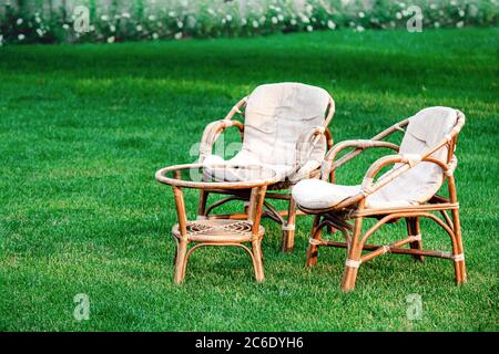 Holzgartenmöbel auf Rasen im Freien zum Entspannen an heißen Sommertagen. Gartenlandschaft mit Rosen und zwei Stühlen in der Natur. Rest im Park Café Stockfoto