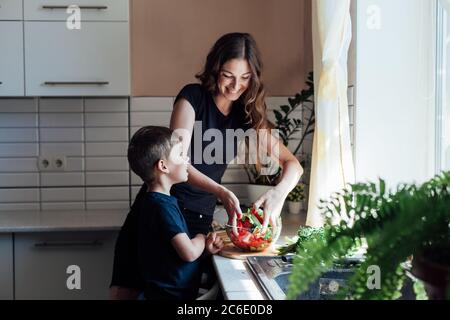 Kleiner Sohn hilft Mama Gemüse Salat in der Küche kochen Stockfoto