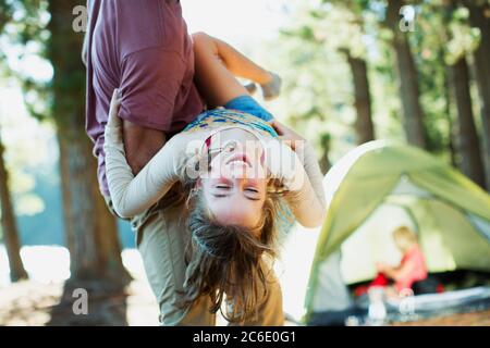 Vater trägt glückliche Tochter außerhalb Zelt in Wäldern Stockfoto