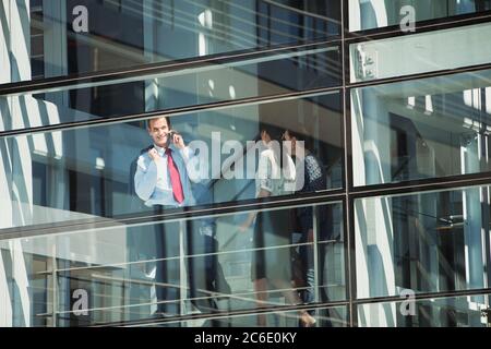 Lächelnder Geschäftsmann, der am Fenster mit dem Handy telefoniert Stockfoto