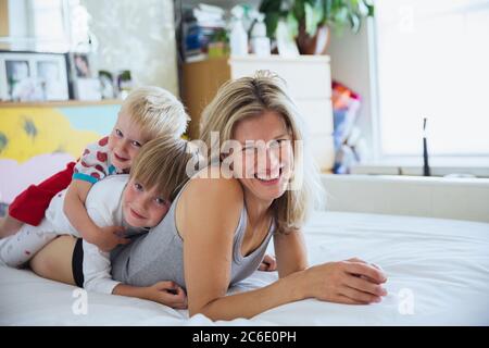 Portrait der Mutter mit Söhnen im Bett, die übereinander liegen Stockfoto