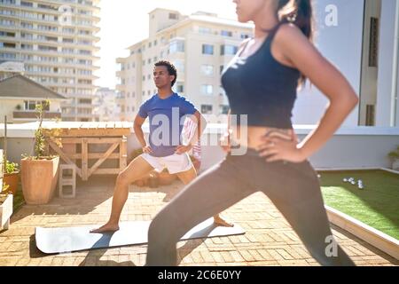 Junges Paar, das Yoga auf dem sonnigen städtischen Dach praktiziert Stockfoto