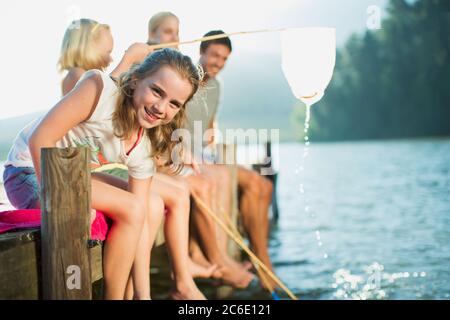 Lächelnde Familie mit Fischernetzen am Dock über dem See Stockfoto