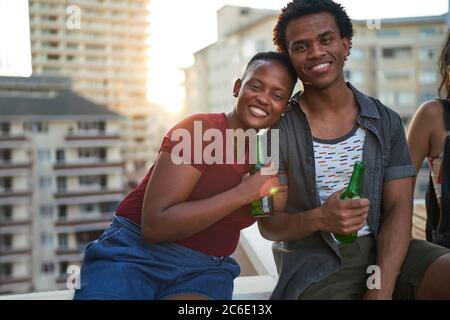 Portrait glückliches junges Paar, das Bier auf dem städtischen Dach trinkt Stockfoto