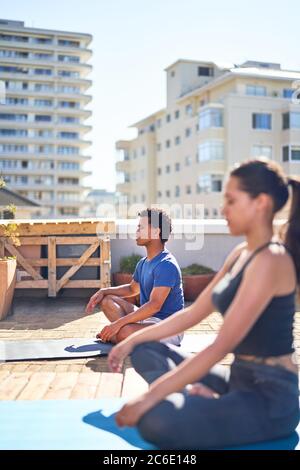 Junge Männer und Frauen üben Yoga auf sonnigem städtischen Dach Stockfoto