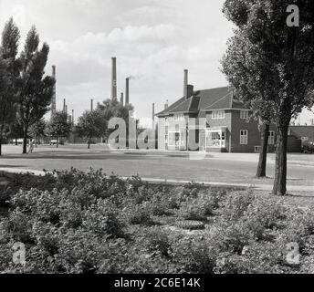 1950er Jahre, historisches Bild des „Co-operative“ Geschäfts und Postamtes im Modelldorf Stewartby in Bedfordshire, dem Standort der London Brick Company, der damals größten Ziegelei der Welt. Im Hintergrund sind mehrere der riesigen Industrieschornsteine aus den Ziegelöfen zu sehen. Die Familie Stewart, die Besitzer von Londoner Ziegeln, waren väterliche Arbeitgeber und stellten ihren großen Arbeitern Wohnungen sowie Sport- und Freizeiteinrichtungen zur Verfügung, was einer Tradition der Quäkerfamilien des vorigen Jahrhunderts entsprach. Stockfoto