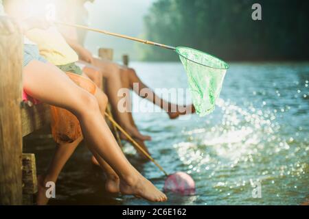 Familie am Dock mit Fischernetzen, die Füße in den See tauchen Stockfoto