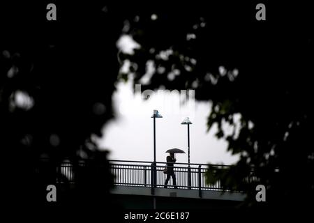 Bremen, Deutschland. Juli 2020. Ein Mann mit einem Schirm geht über eine Brücke. Quelle: Sina Schuldt/dpa/Alamy Live News Stockfoto