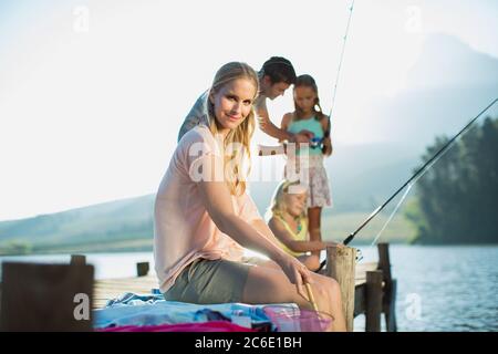 Lächelnde Frau mit Familie Angeln auf Dock über See Stockfoto