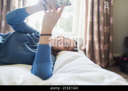 Glückliches Teenager-Mädchen mit Smartphone auf dem Bett Stockfoto