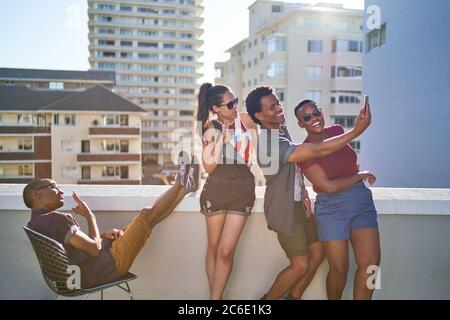 Glückliche junge Freunde, die Selfie auf dem sonnigen städtischen Balkon machen Stockfoto