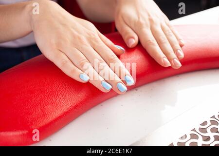 Das Endergebnis der Maniküre. Schöne blaue Nägel. Der Prozess der Maniküre in einem Schönheitssalon. Salon in schwarz, rot, weiß. Stockfoto