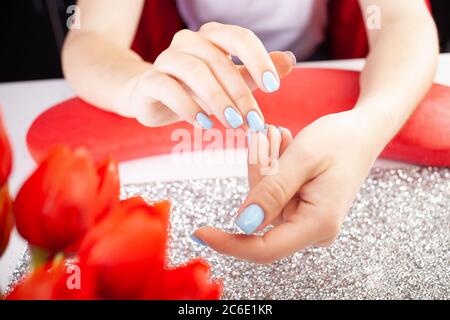 Das Endergebnis der Maniküre. Schöne blaue Nägel. Der Prozess der Maniküre in einem Schönheitssalon. Salon in schwarz, rot, weiß. Stockfoto